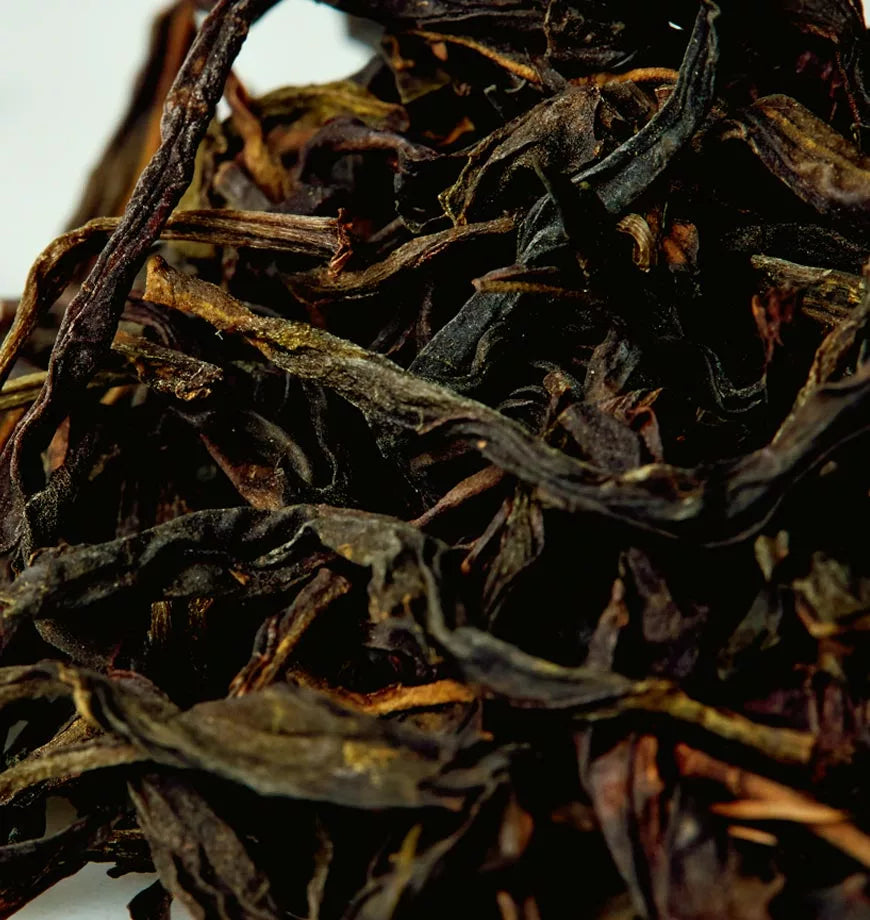 A pile of dried black tea leaves labeled Golden Phoenix on a white surface, showcasing their rich, dark color.