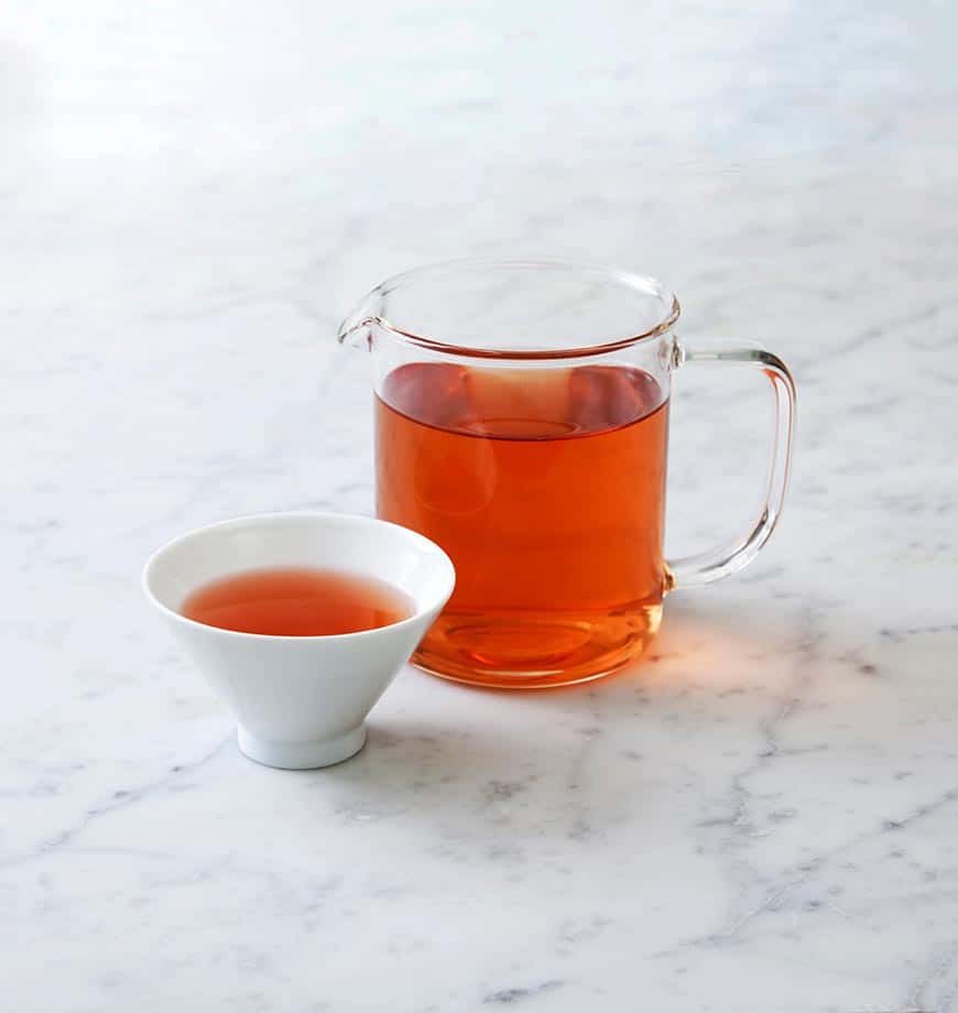 A pitcher of Schizandra berry tea and a cup sit on a marble counter, showcasing a warm herbal infusion.