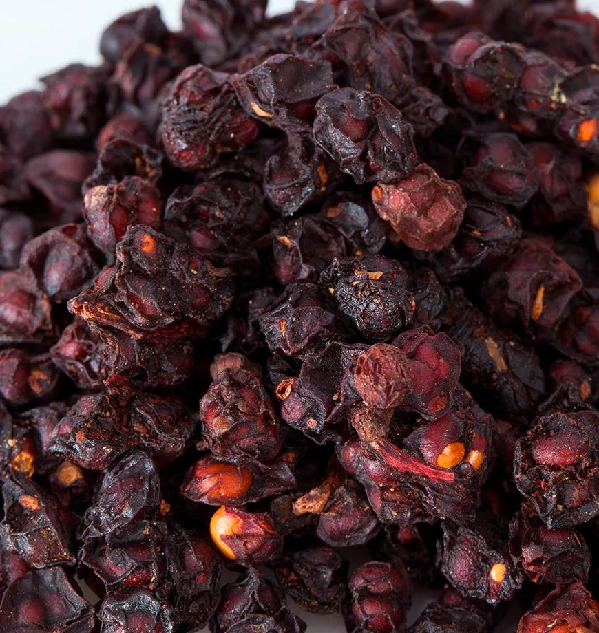 Dried red peppers stacked on a white background, highlighting their rich color, often used in herbal infusions.