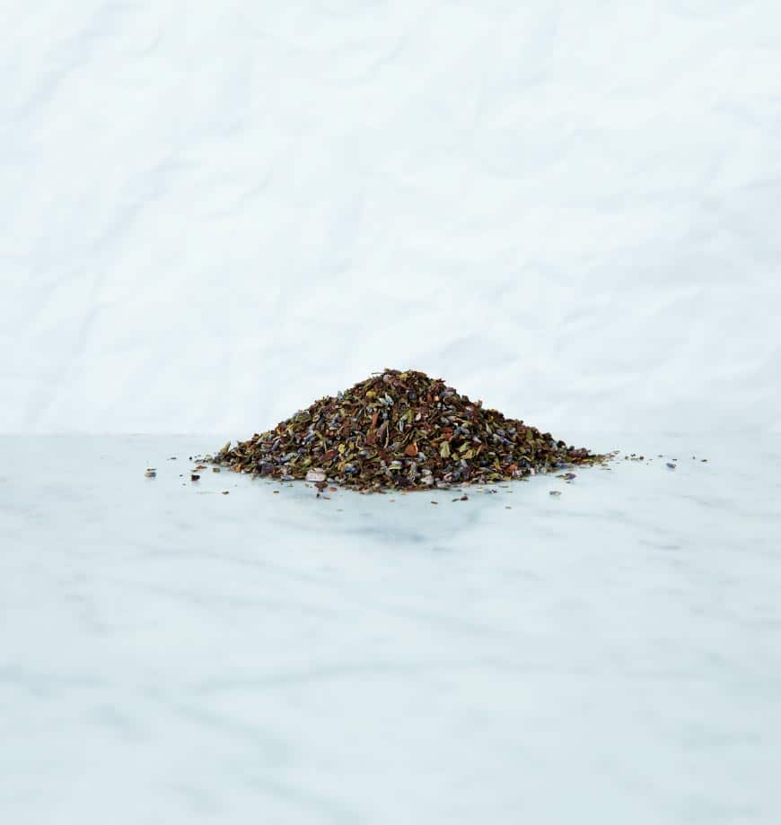 A pile of dried cacao mint herbs on a white surface, showcasing their rich green color and textured leaves.
