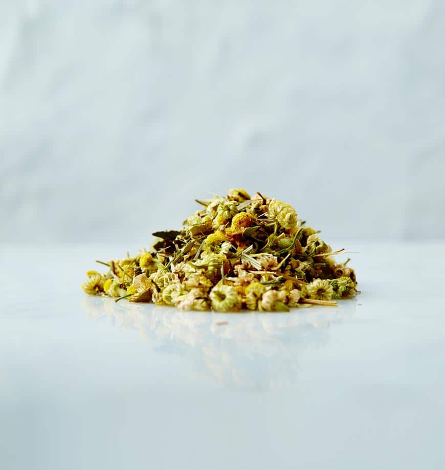 A pile of dried chamomile herbs on a white surface, showcasing their delicate leaves and flowers.