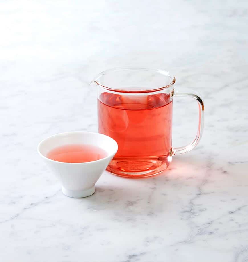 A pitcher of pink Cranberry Eucalyptus tea beside a cup, showcasing a refreshing herbal infusion.