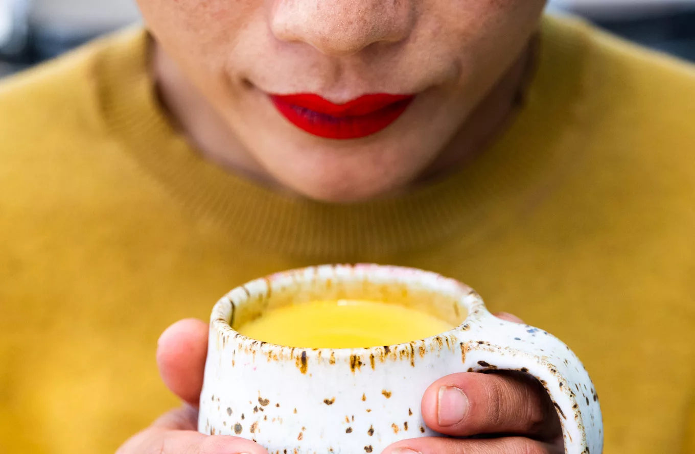 A woman poses with a yellow chai mug, showcasing her vibrant style.