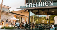 People seated outside Erewhon restaurant, showcasing the exterior and a sign that Samovar tea is now available.
