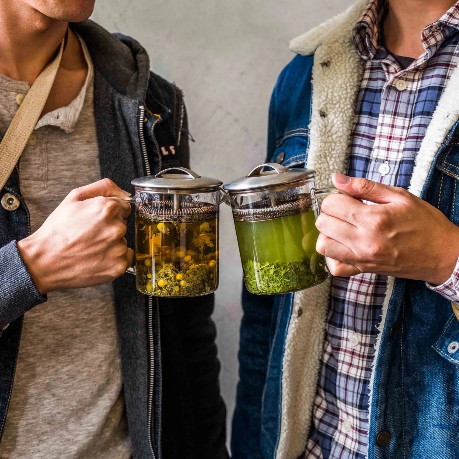 Two men smiling while holding up mugs of tea, celebrating a moment together.