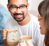 A cheerful man and woman hold tea cups, smiling warmly in a relaxed atmosphere.