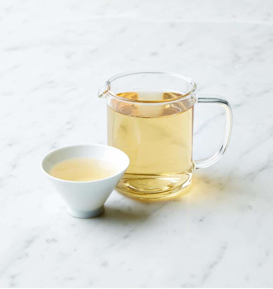A cup of moon bud tea and a pitcher of tea placed on a polished marble counter.