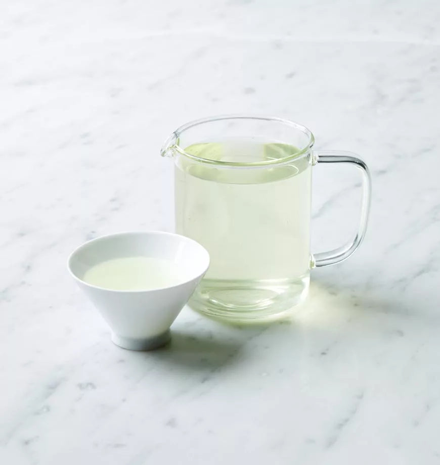 A glass pitcher of organic Nishi Sencha green tea next to a bowl of the tea, highlighting its rich green hue.