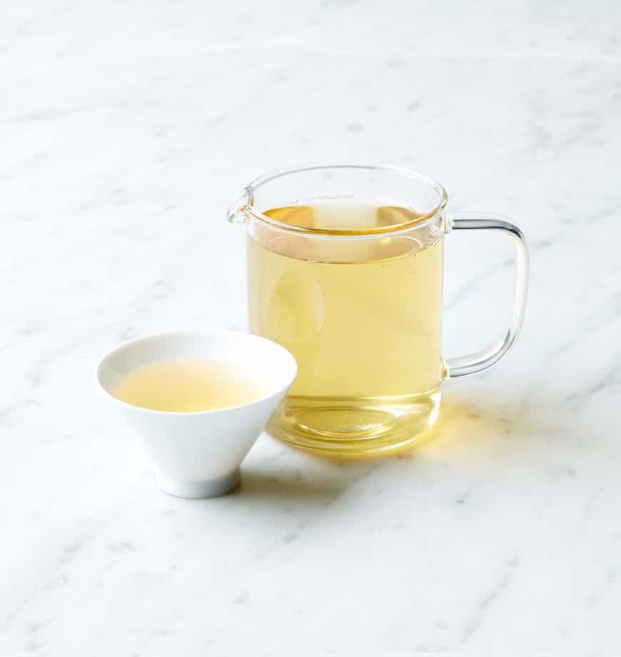 A pitcher of jasmine pearl green tea beside a delicate cup filled with the same fragrant tea.