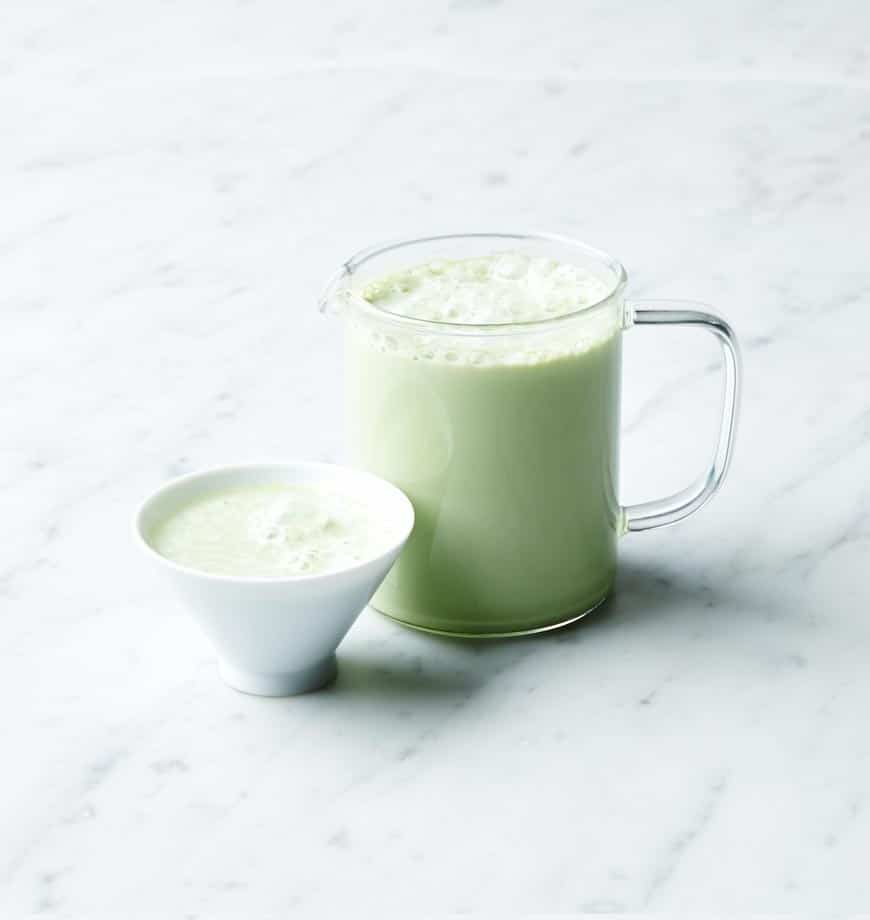 A pitcher of sweet matcha green tea beside a bowl filled with matcha green tea leaves.