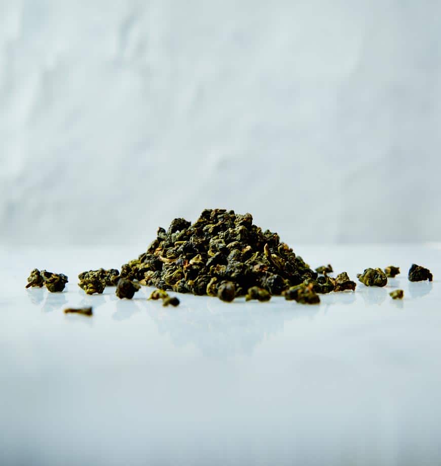 A mound of green tea leaves resting on a white surface, highlighting the fresh, vibrant hues of Four Seasons oolong tea.