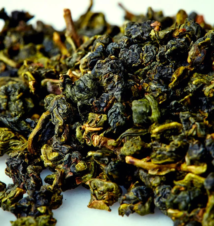 A pile of green tea leaves on a white surface, showcasing the fresh, vibrant color of Four Seasons oolong tea.