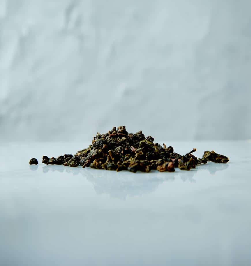 A pile of green tea leaves on a white surface, showcasing the Iron Goddess of Mercy oolong tea variety.
