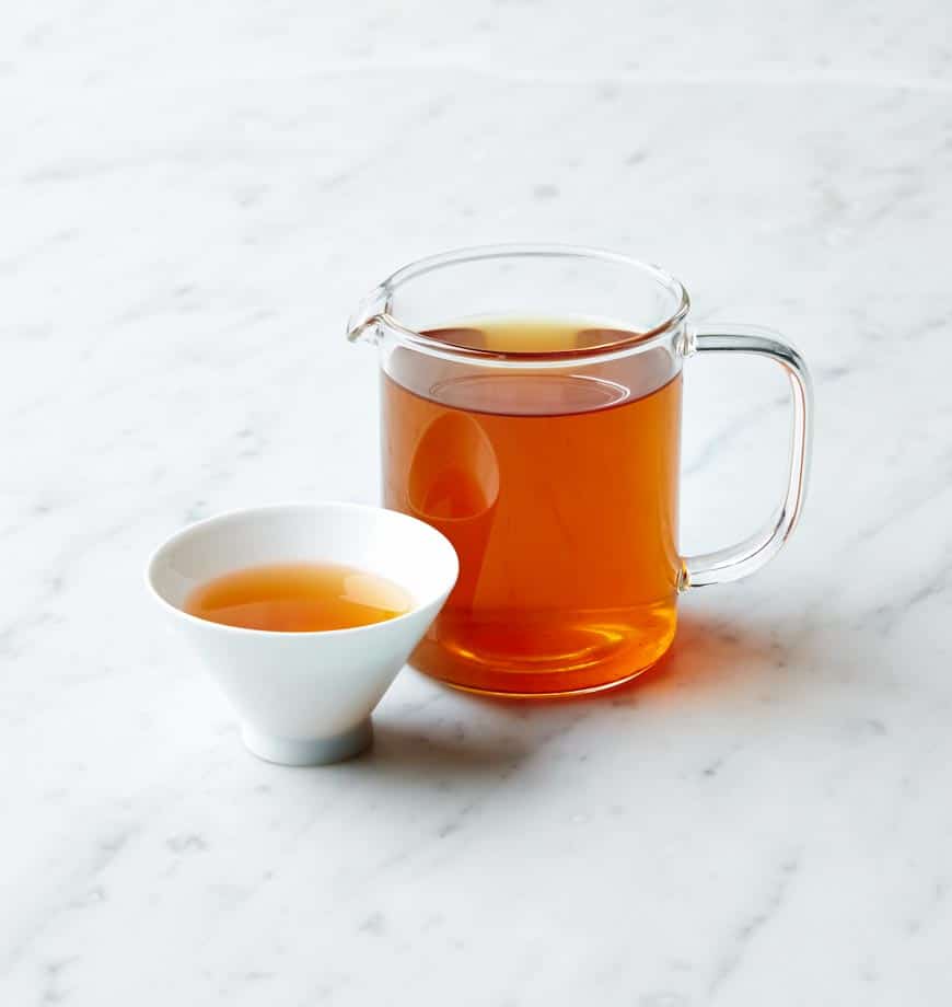 A cup and pitcher of Golden Phoenix tea sit on a polished marble counter, showcasing a warm setup.