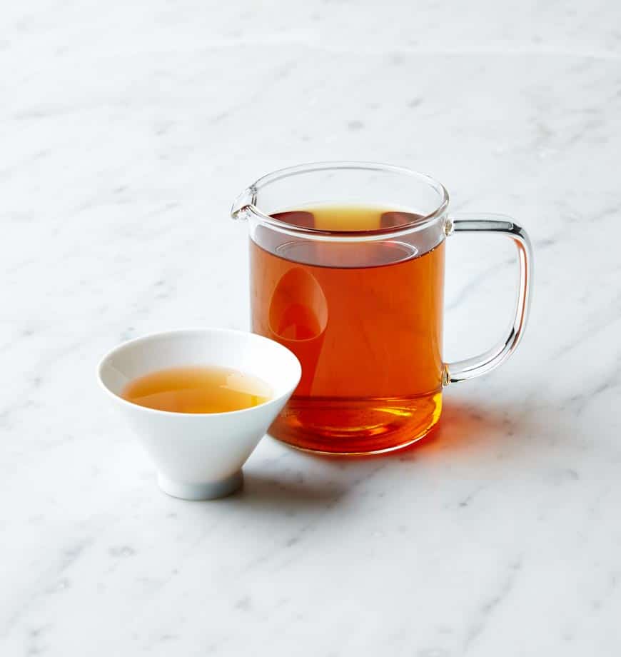 A cup of Wuyi Dark Roast oolong tea beside a pitcher of tea on a polished marble counter.