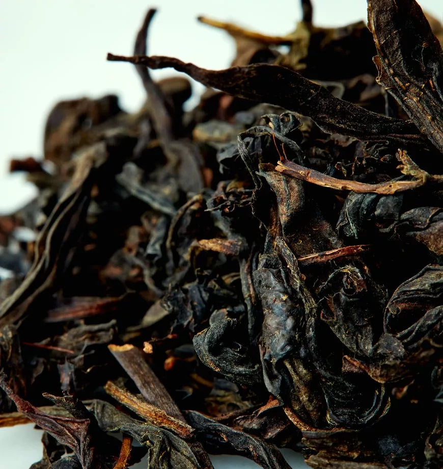 A pile of Wuyi Dark Roast oolong tea leaves on a white surface, showcasing their rich, dark color and texture.