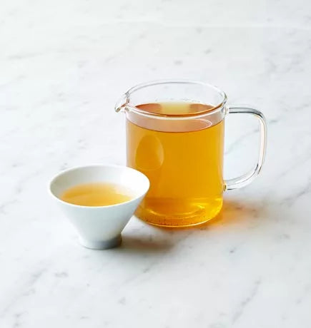 A glass pitcher filled with Apple Ginseng oolong tea beside a small bowl of loose tea leaves.