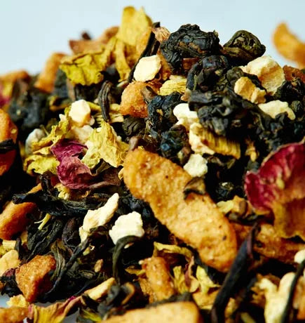 A white plate holds a colorful pile of dried fruit and nuts, accompanied by a cup of Apple Ginseng tea nearby.