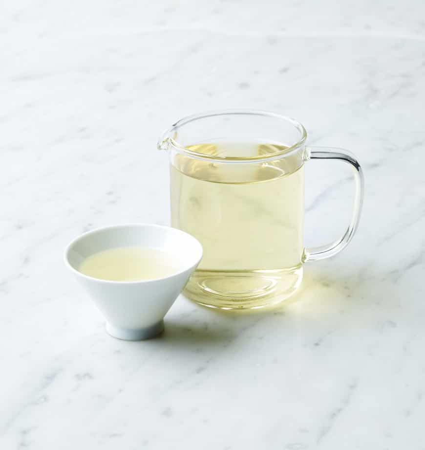 A pitcher of green tea beside a bowl of white tea, featuring Pineapple Coconut oolong tea leaves.