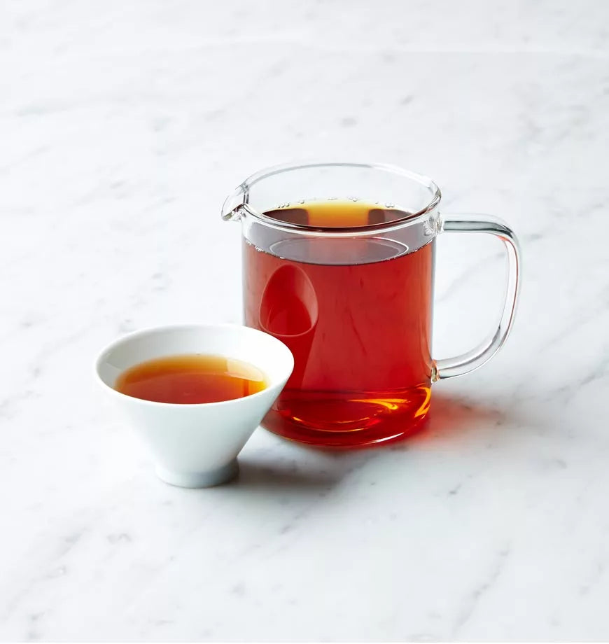 A cup of black tea and a pitcher of tea sit on a marble counter, showcasing a warm and inviting beverage setup