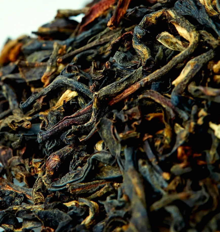 A close-up of black tea powder mixed with brown leaves, showcasing its rich texture and color