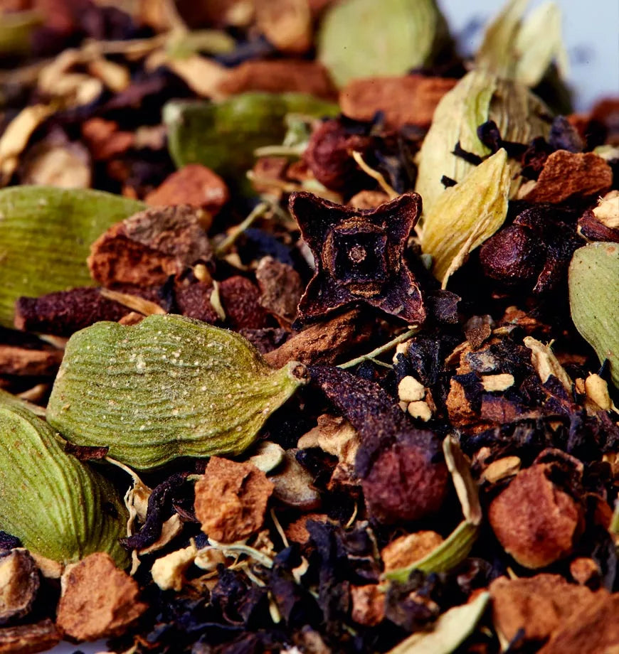 A pile of spices and nuts on a white surface, representing ingredients for organic masala chai tea.