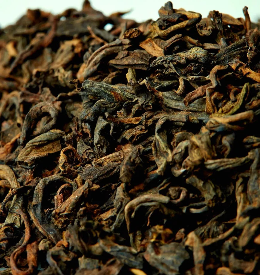 A close-up of a pile of dried black tea leaves labeled as Maiden's Ecstasy Tea Leaf, showcasing their rich, dark color.