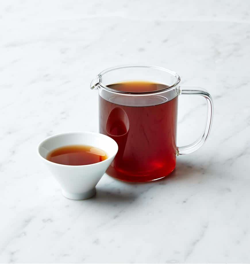 A cup of Blood Orange Tea and a pitcher of the same tea on a polished marble counter.