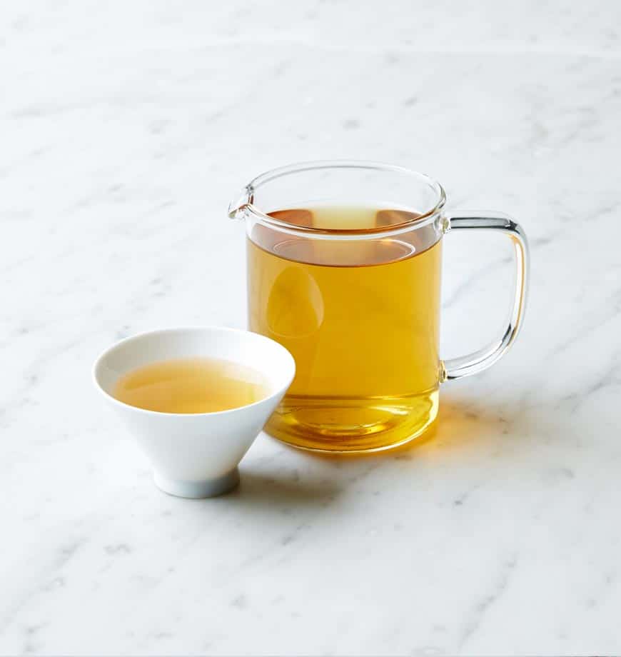 A cup of Cacao Mint herbal tea and a pitcher of tea on a polished marble counter.