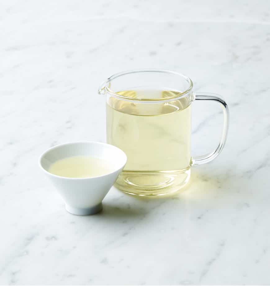 A glass pitcher beside a cup of green tea labeled Chamomile Twist, an herbal infusion.