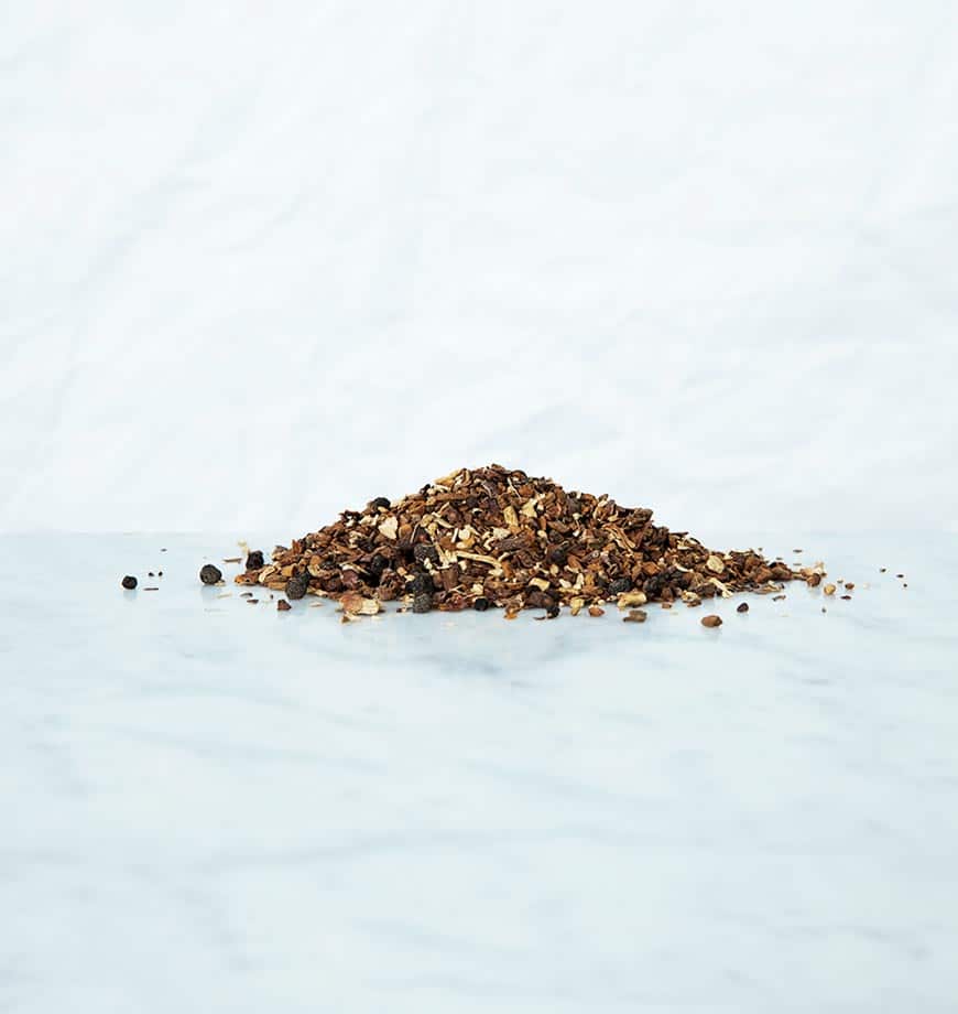A pile of brown and black spices on a white surface, representing ingredients for Dandelion Detox tea