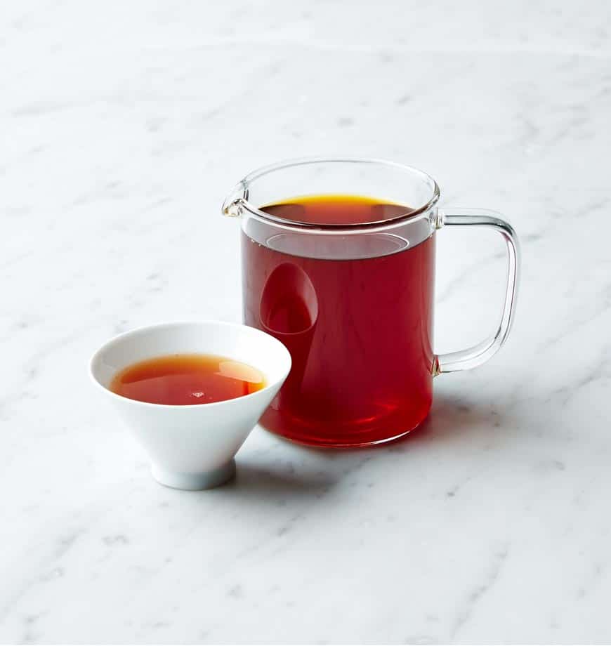 A cup and pitcher of Rooibos Earl Grey tea displayed on a sleek marble countertop.