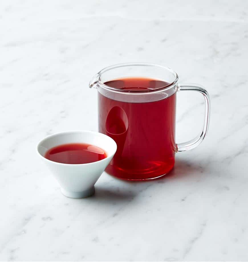 A pitcher of red tea labeled Hibiscus Bliss sits next to a bowl containing a matching red liquid.