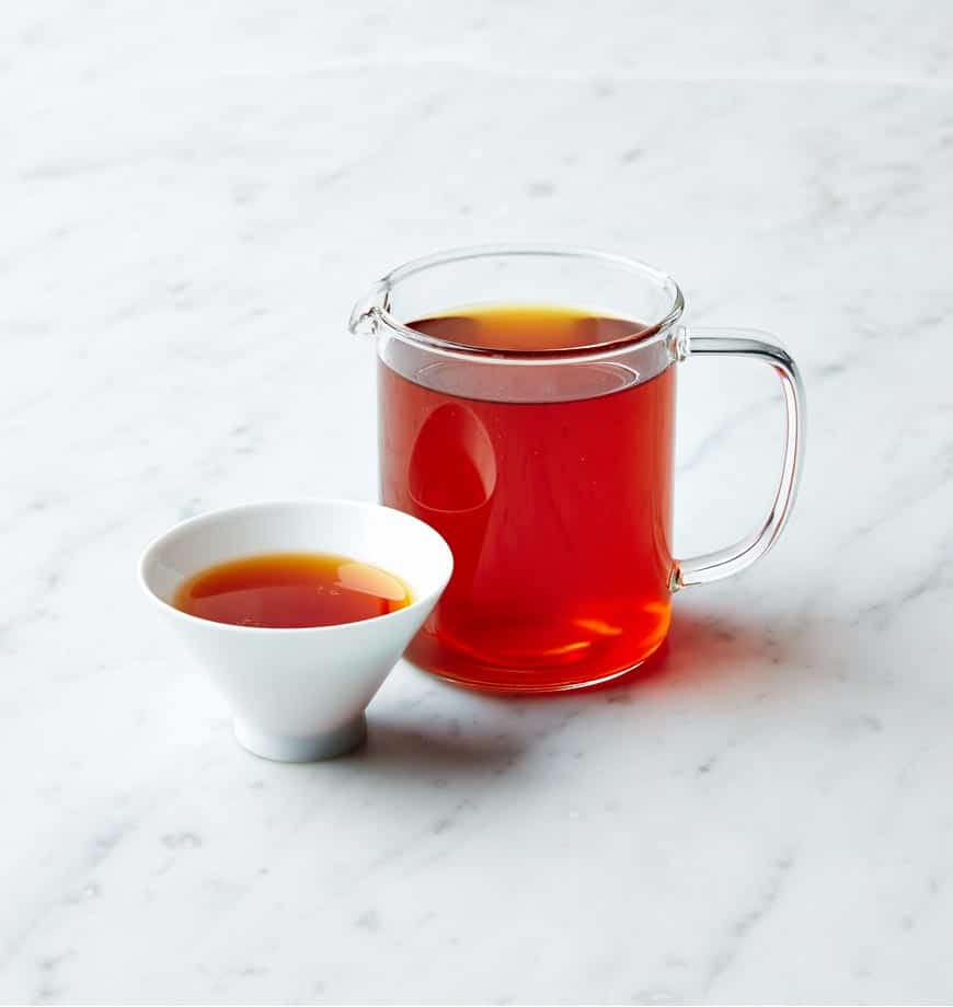 A marble counter displays a pitcher and cup of Rooibos Ocean of Wisdom herbal tea, creating a cozy tea-drinking scene.