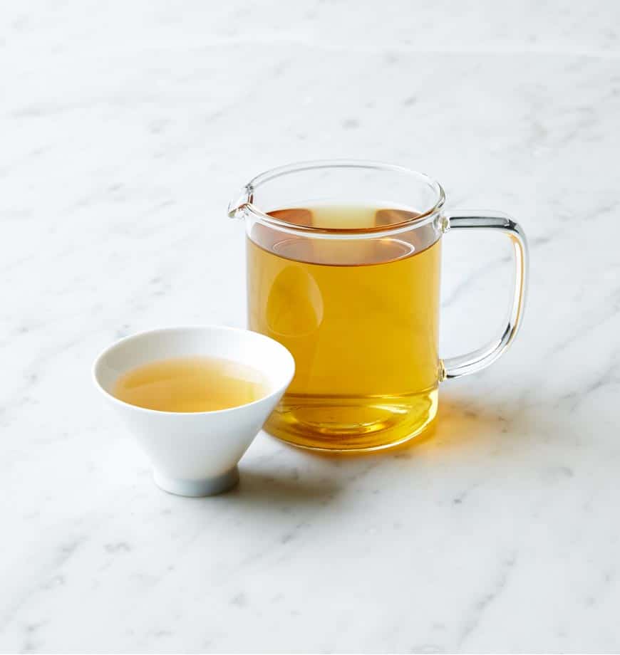 A cup and pitcher of Spearmint Sage herbal tea placed on a polished marble counter.