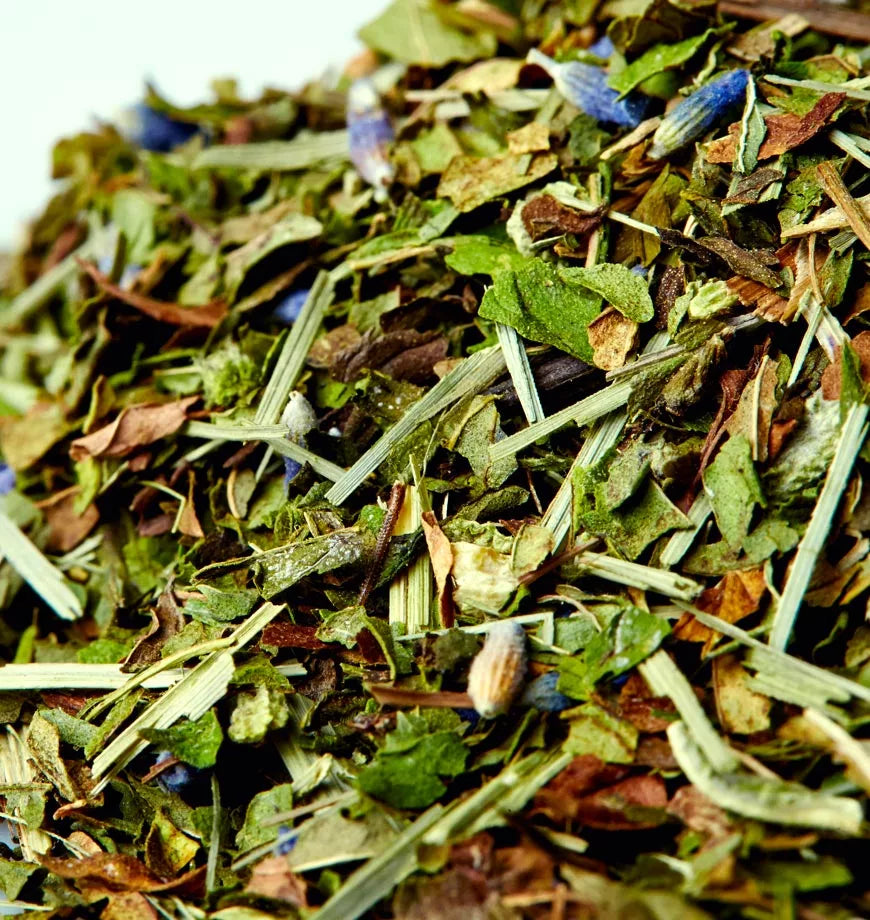 A pile of dried spearmint and sage leaves on a white surface, ready for herbal infusion.