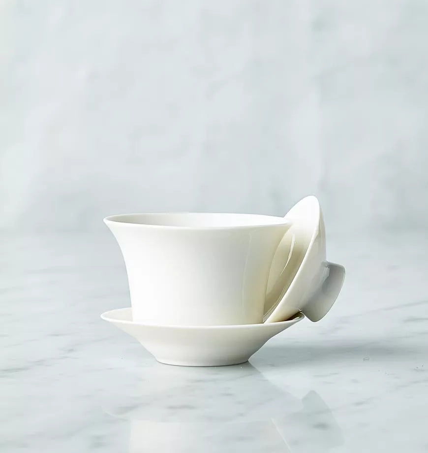 A covered white cup and saucer resting on a marble countertop.