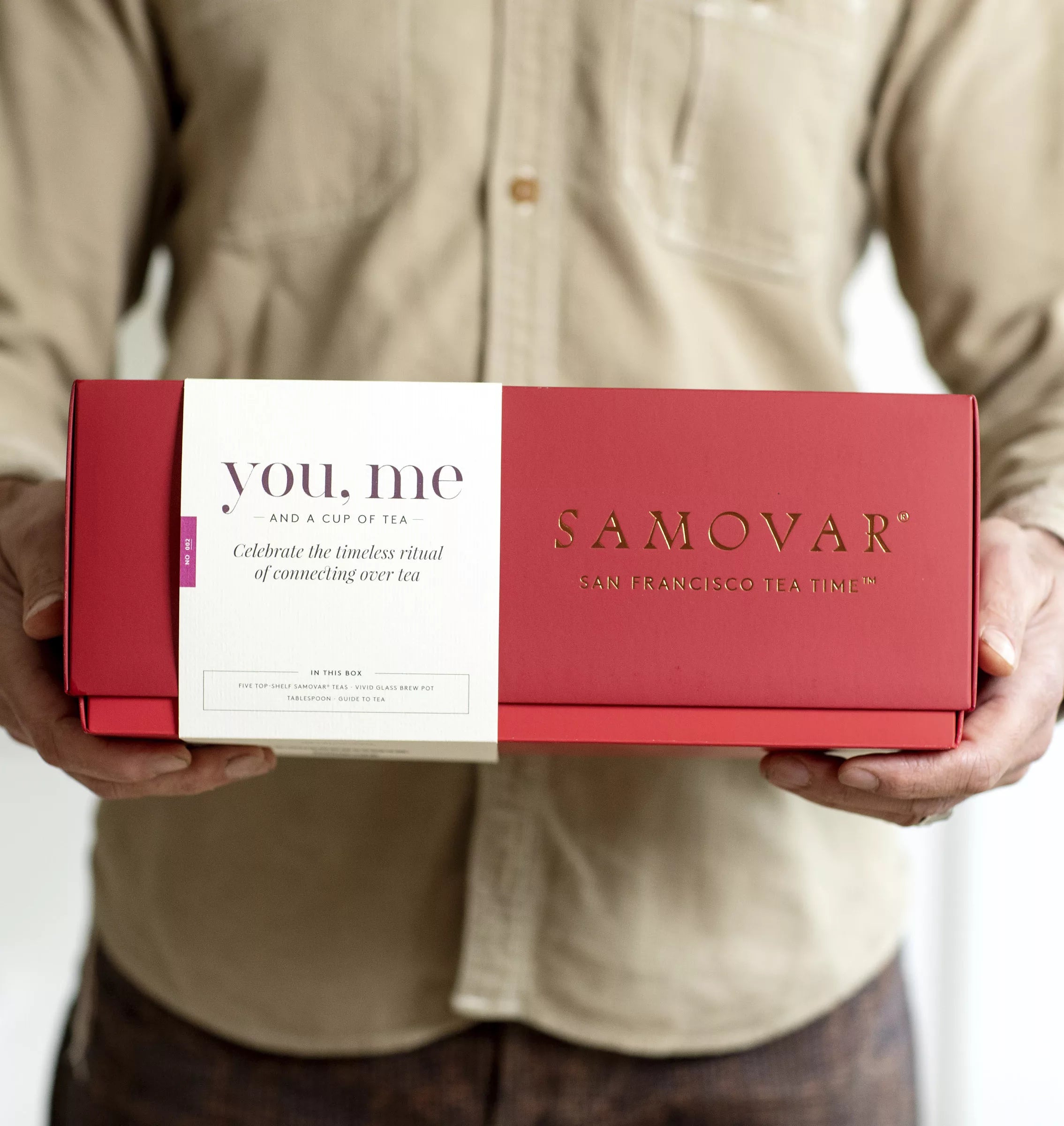 A man holding a box of samovar wine, showcasing an organic tea gift set with elegant packaging.