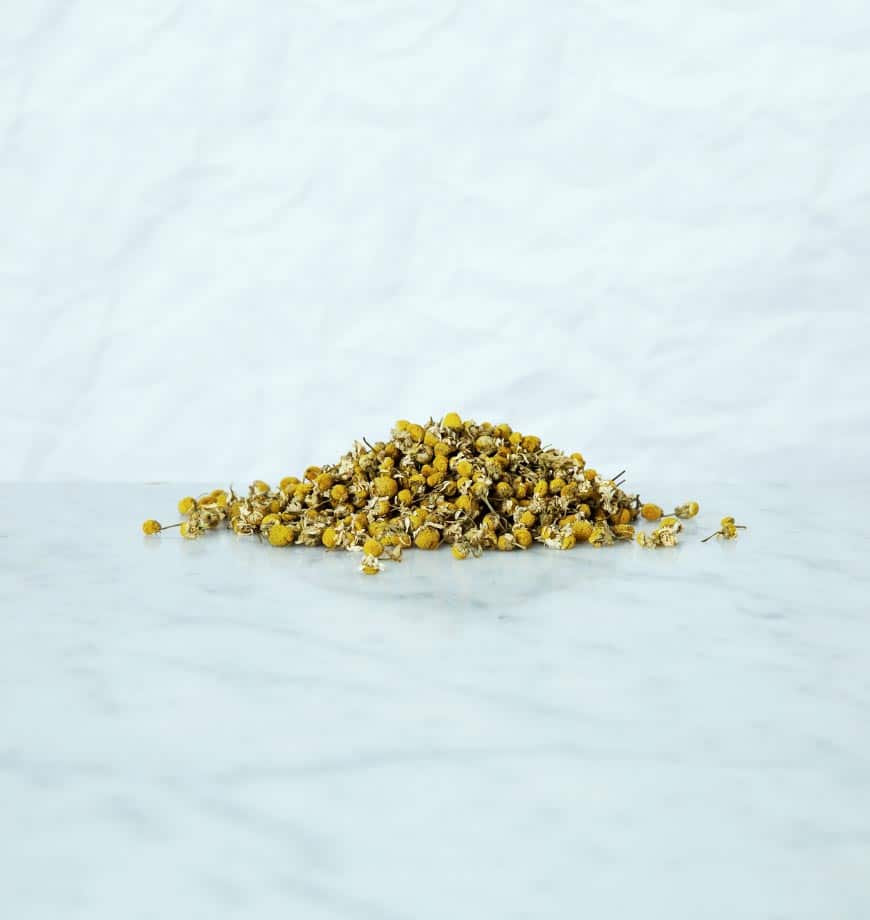 Dried chamomile flowers arranged on a white surface, ideal for brewing herbal tea