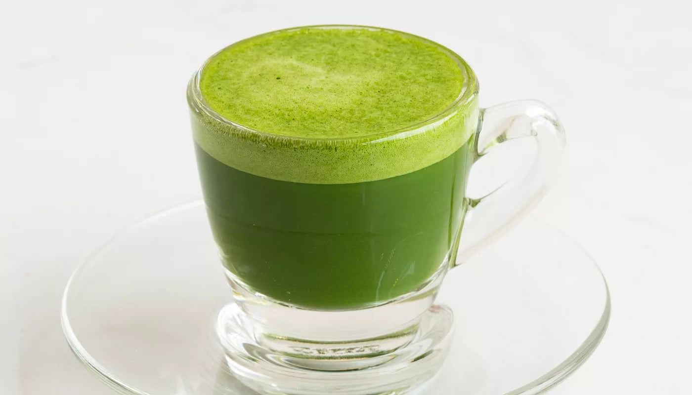 A glass of organic green tea on a saucer, featuring Shibumi Matcha branding.