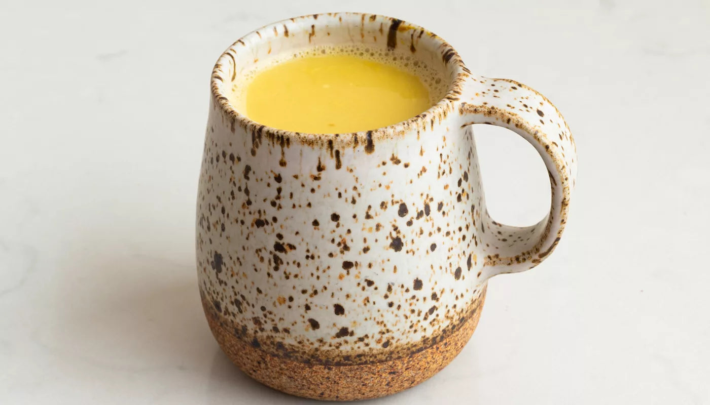 A white surface supports a mug containing a bright yellow herbal infusion, identified as turmeric tonic.