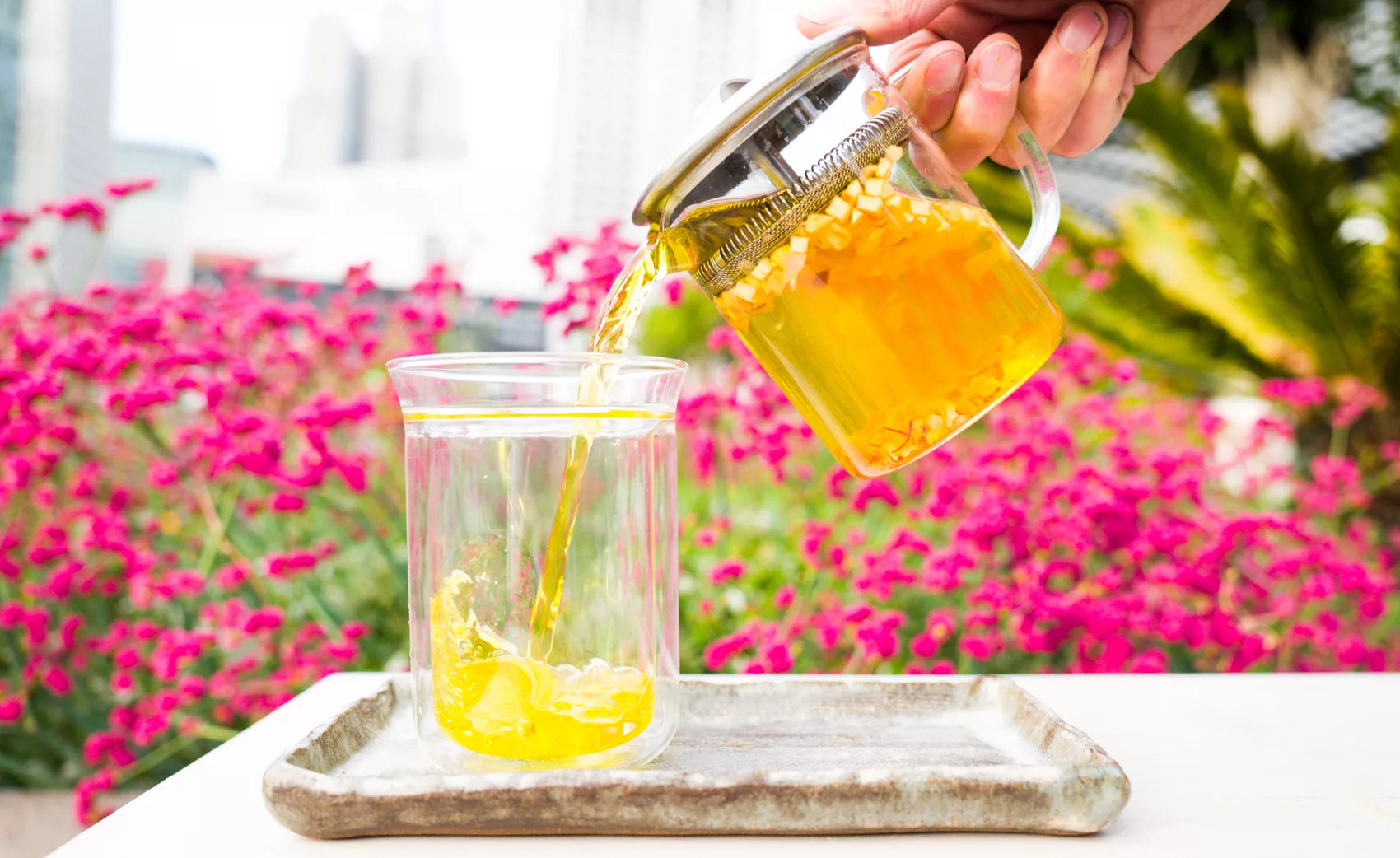 A person pouring fresh tea from a Vivid Brew glass infuser teapot into a clear glass.