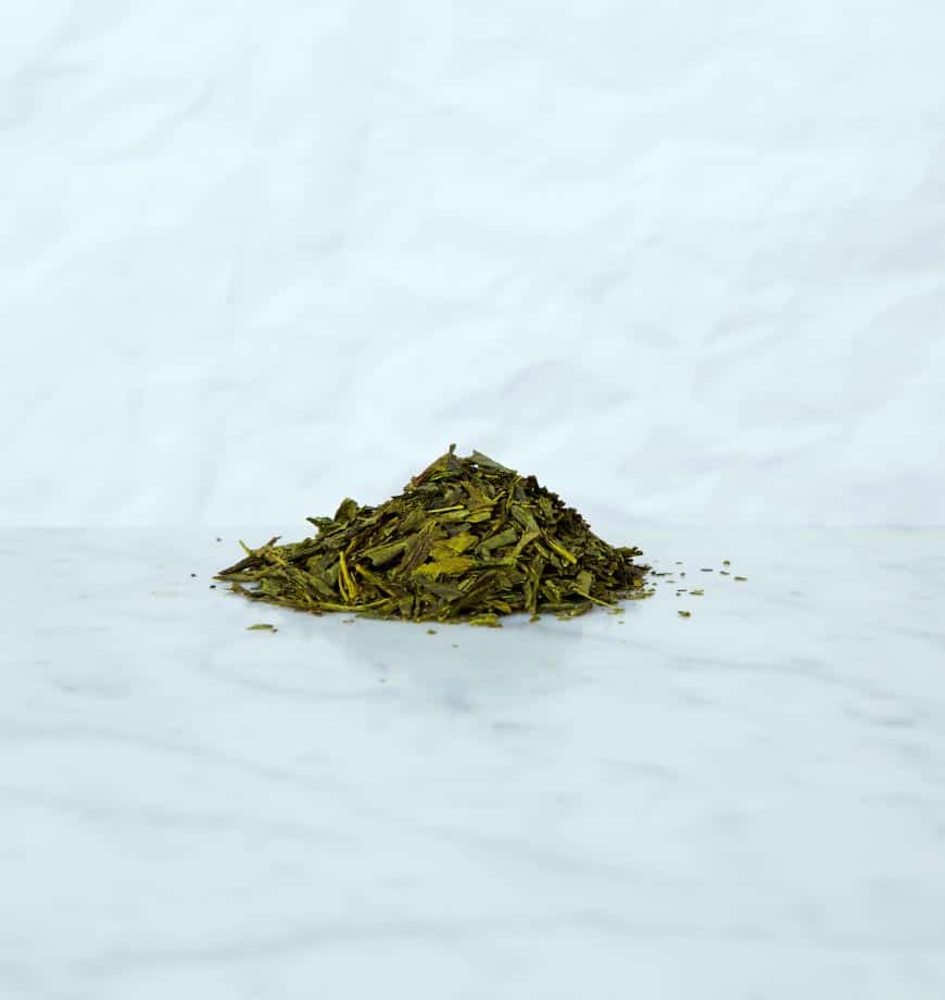 A pile of Bancha green tea leaves on a clean white surface, showcasing their vibrant green color and texture.