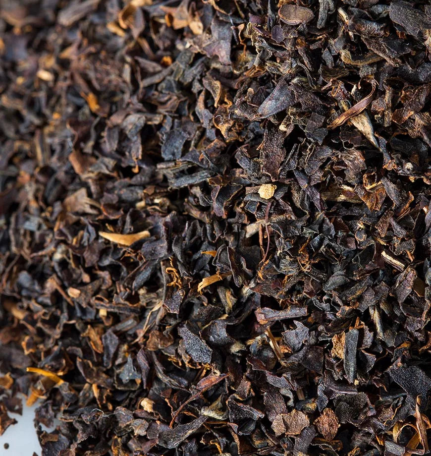 A pile of black tea leaves on a white surface, showcasing the rich texture and color of black iced tea ingredients.