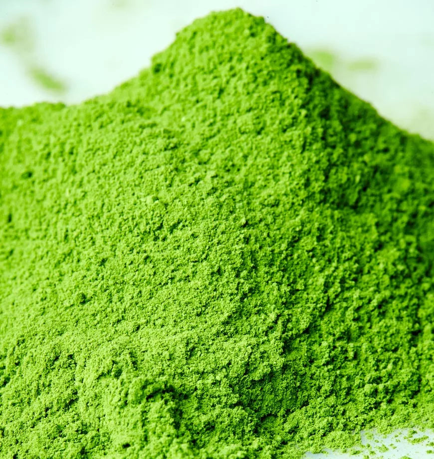 A pile of vibrant green matcha powder on a clean white surface, labeled as Shibumi Matcha, organic green tea.