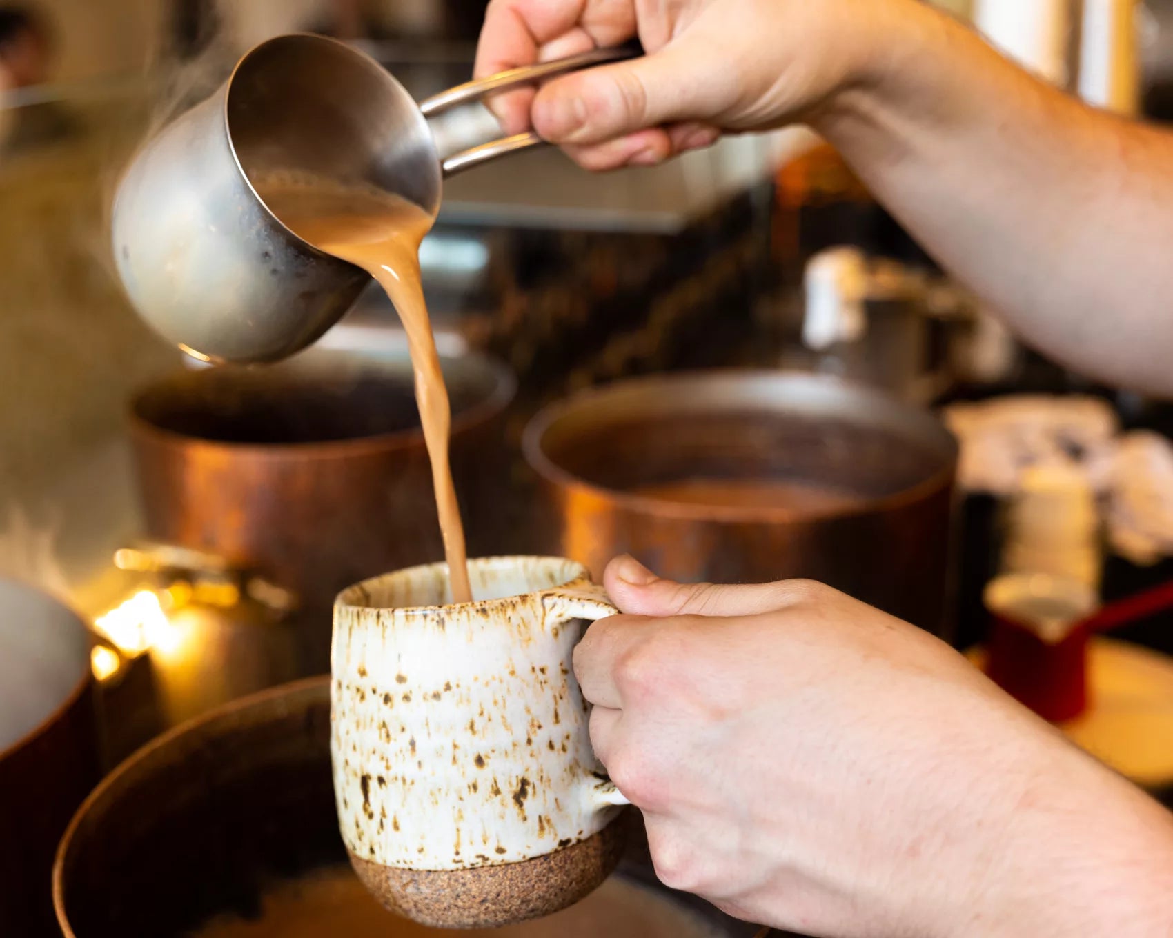 A person pouring freshly brewed tea from a pot into a white mug on a wooden table.