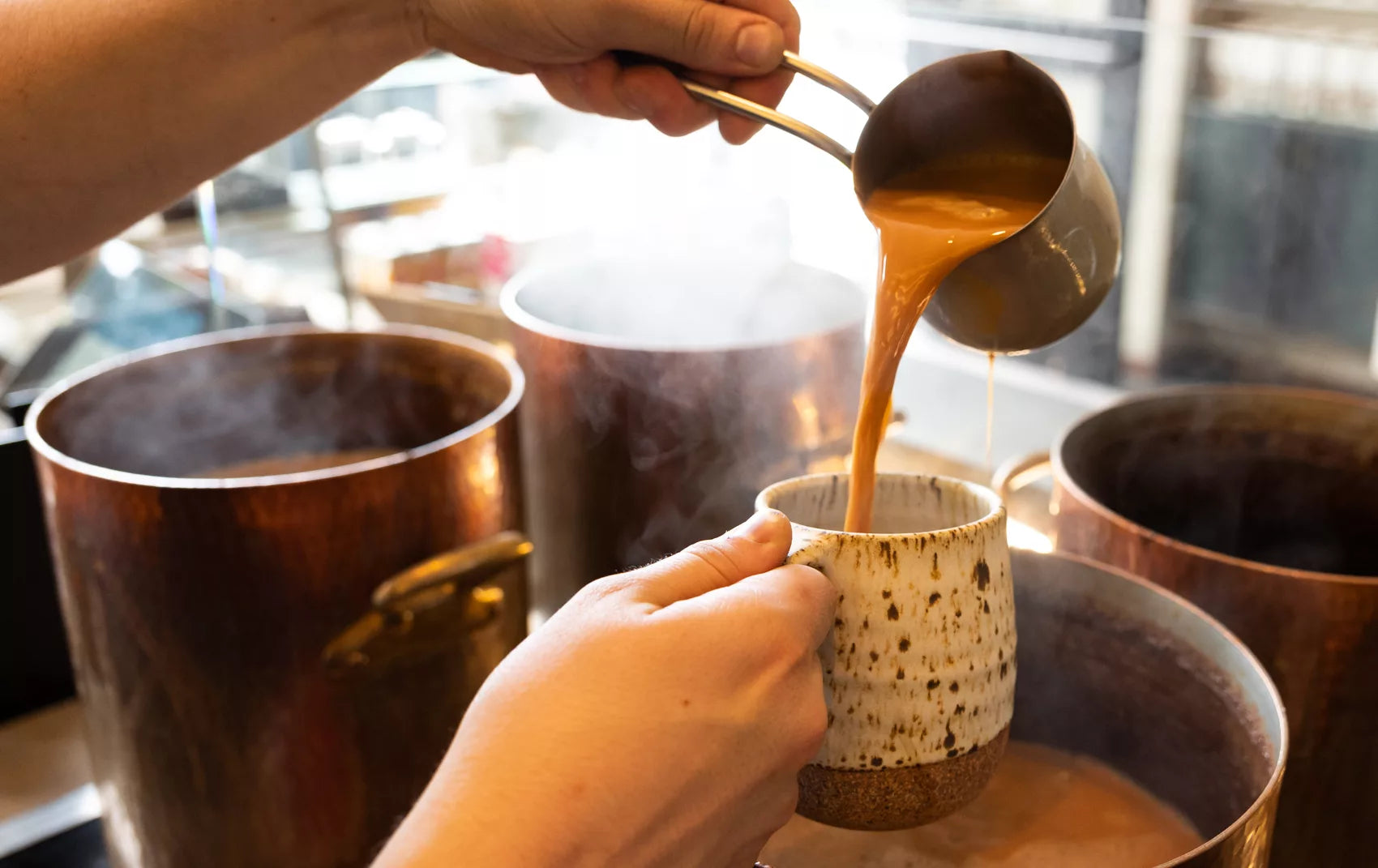 A hand pours Pumpkin Chai into a mug, with steam visible, highlighting the warm and inviting drink.