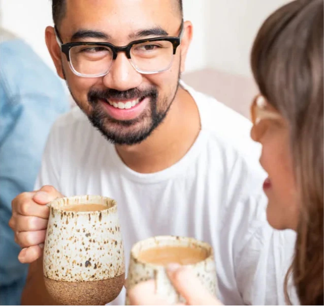 A cheerful man and woman hold tea cups, smiling warmly in a relaxed atmosphere.